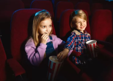Deux enfants assis sur des sièges rouges mangent du pop-corn
